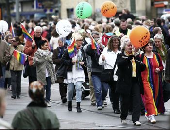 bild från prideparad med glada människor som bär ballonger och regnbågsflaggor.